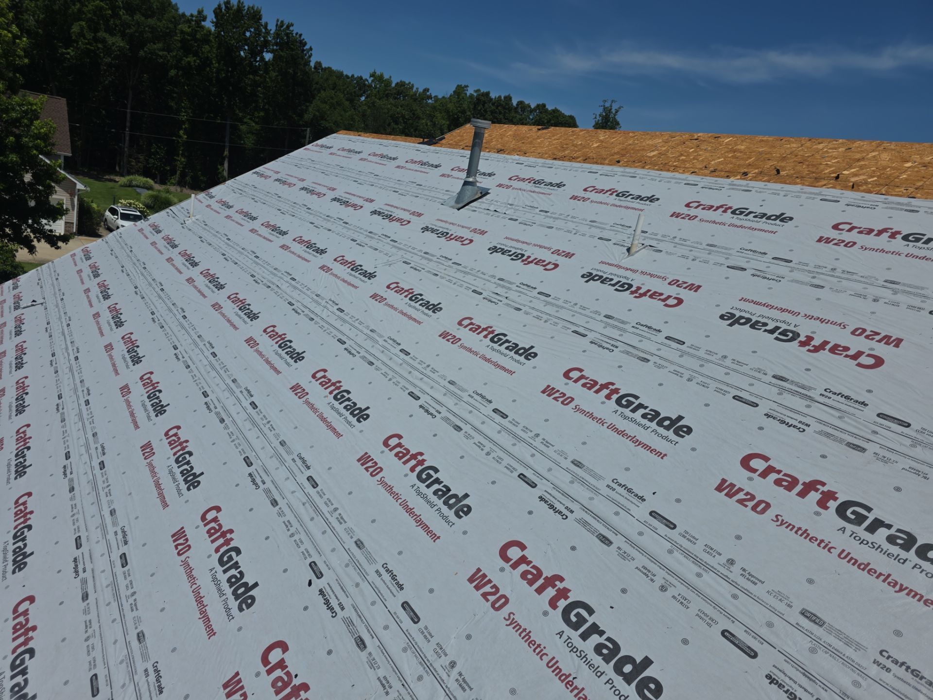Roof under construction with white synthetic underlayment and a vent pipe on a sunny day