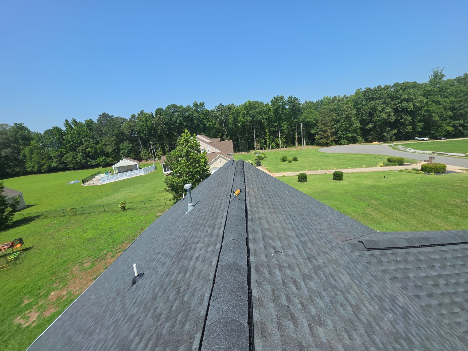 View from a shingled roof overlooking green fields, trees, and a clear blue sky
