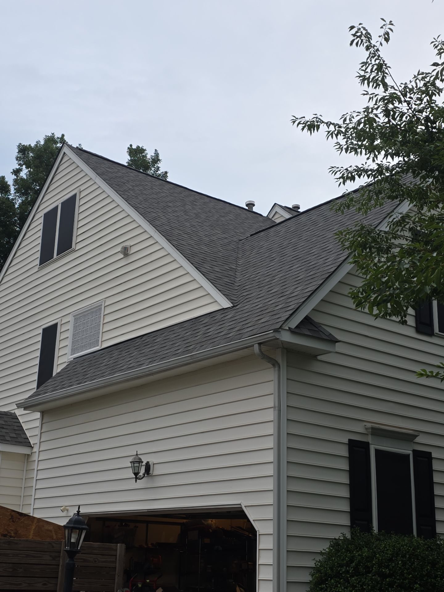 White-sided house with gray roof and gables, viewed from the side with trees and cloudy sky.