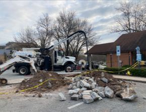 A white truck is driving down a street next to a pile of rocks