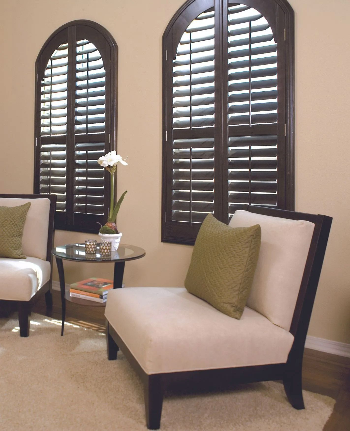 A living room with two chairs and two windows with shutters
