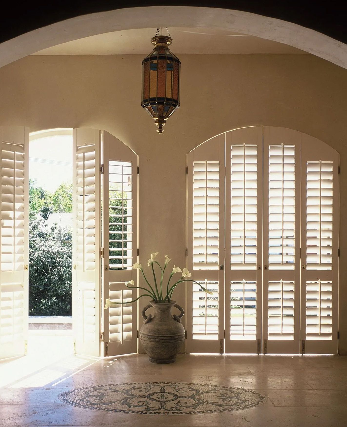 A room with white shutters and a vase of flowers