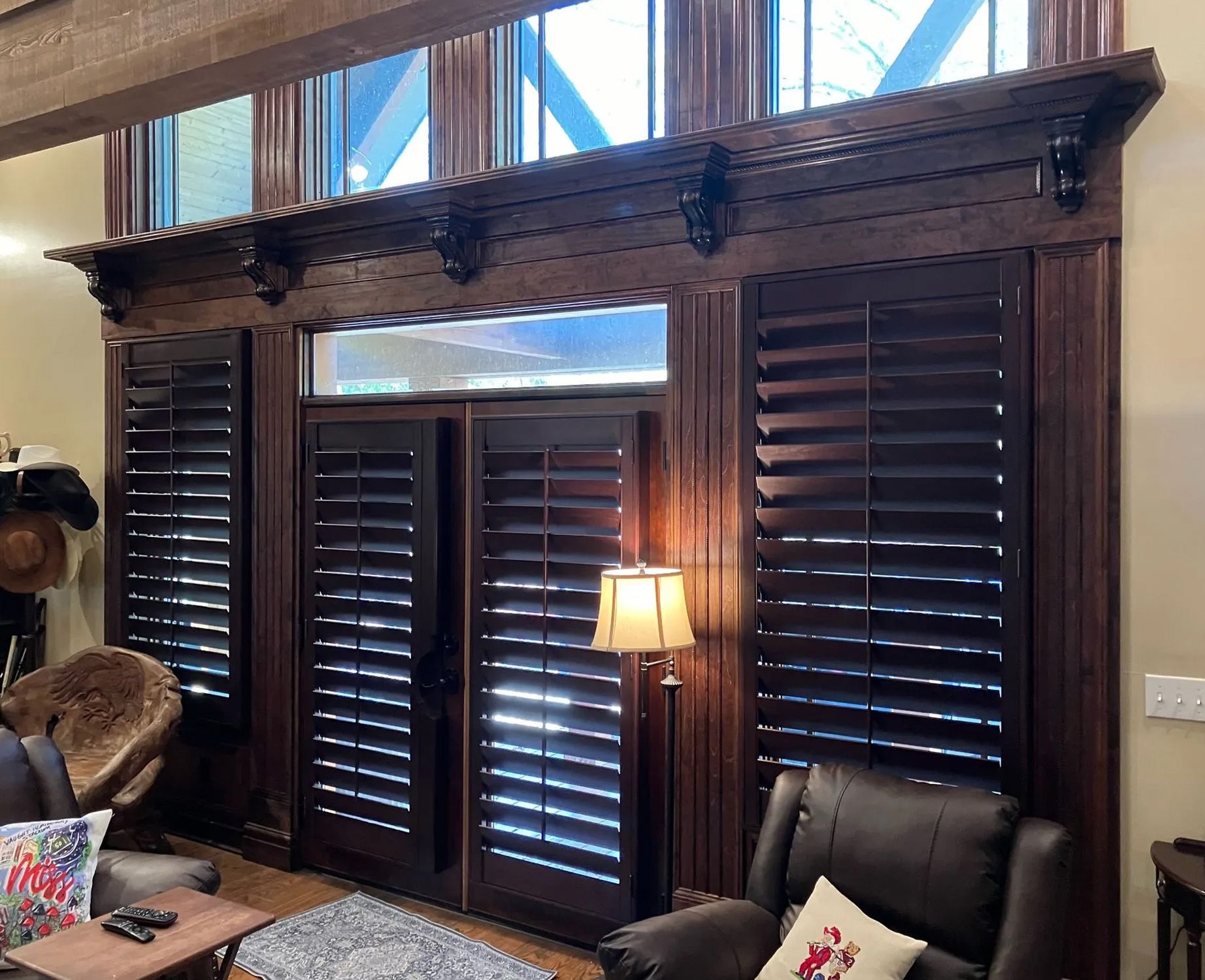 A living room with a chair , table , lamp and shutters on the windows.