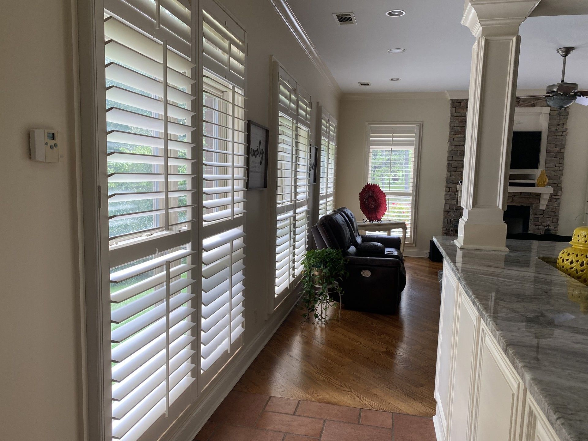 A bright hallway with white shutters on the windows, leading to a seating area and a living room.