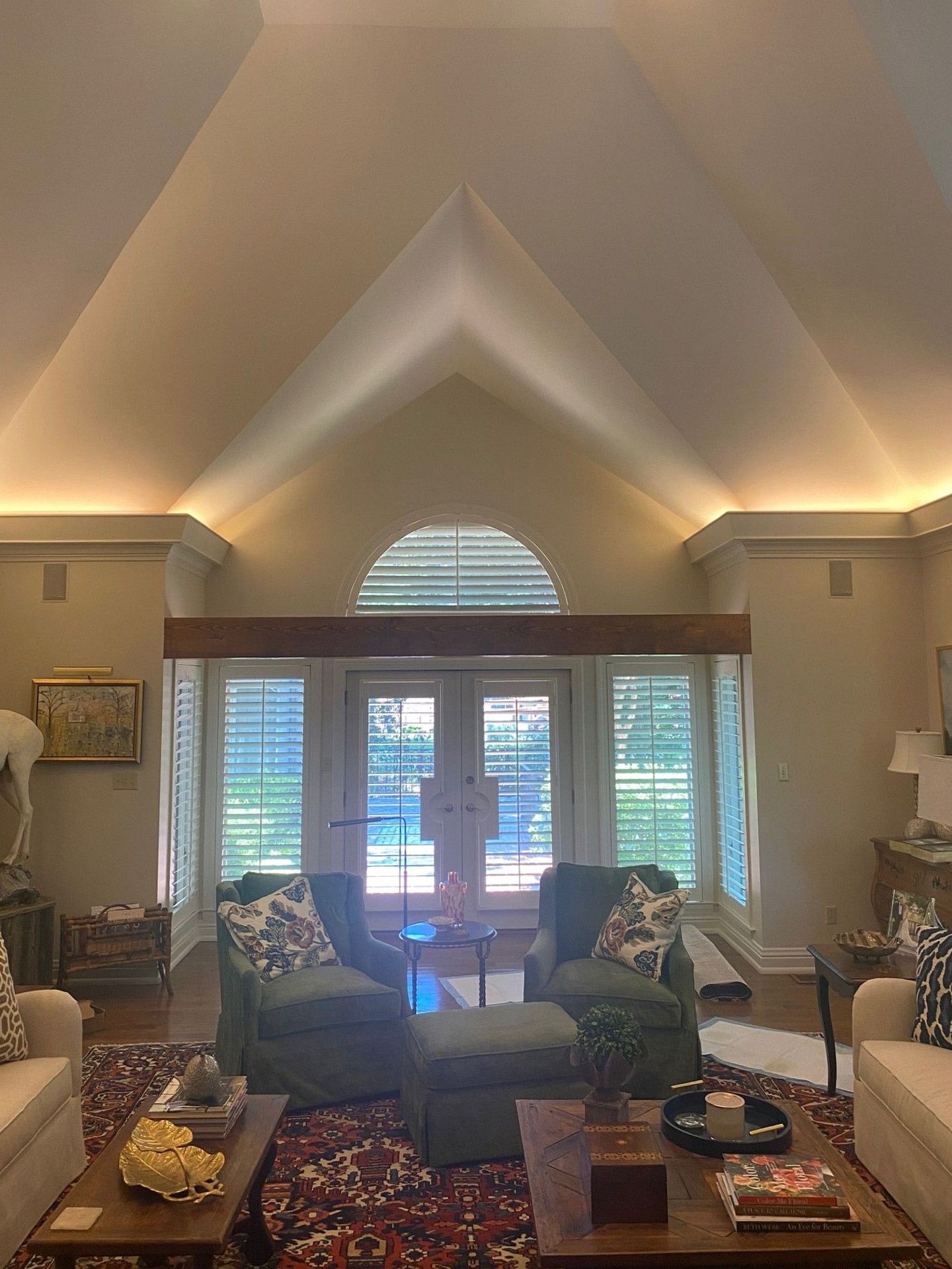 A bright, vaulted-ceiling living room with shuttered windows and two green armchairs facing a glass door.