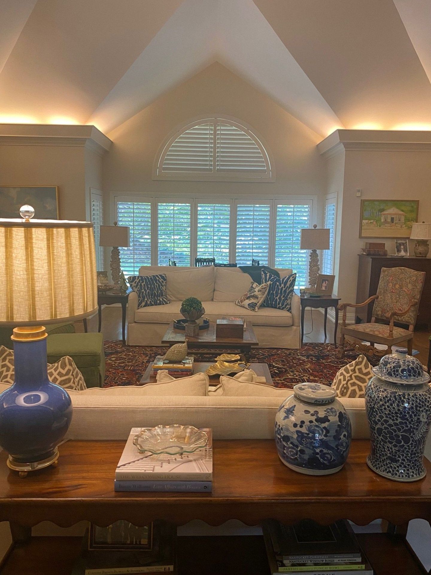 Living room with vaulted ceiling, white sofa, blue and white patterned throw pillows and ginger jars, and a wooden table in the foreground.