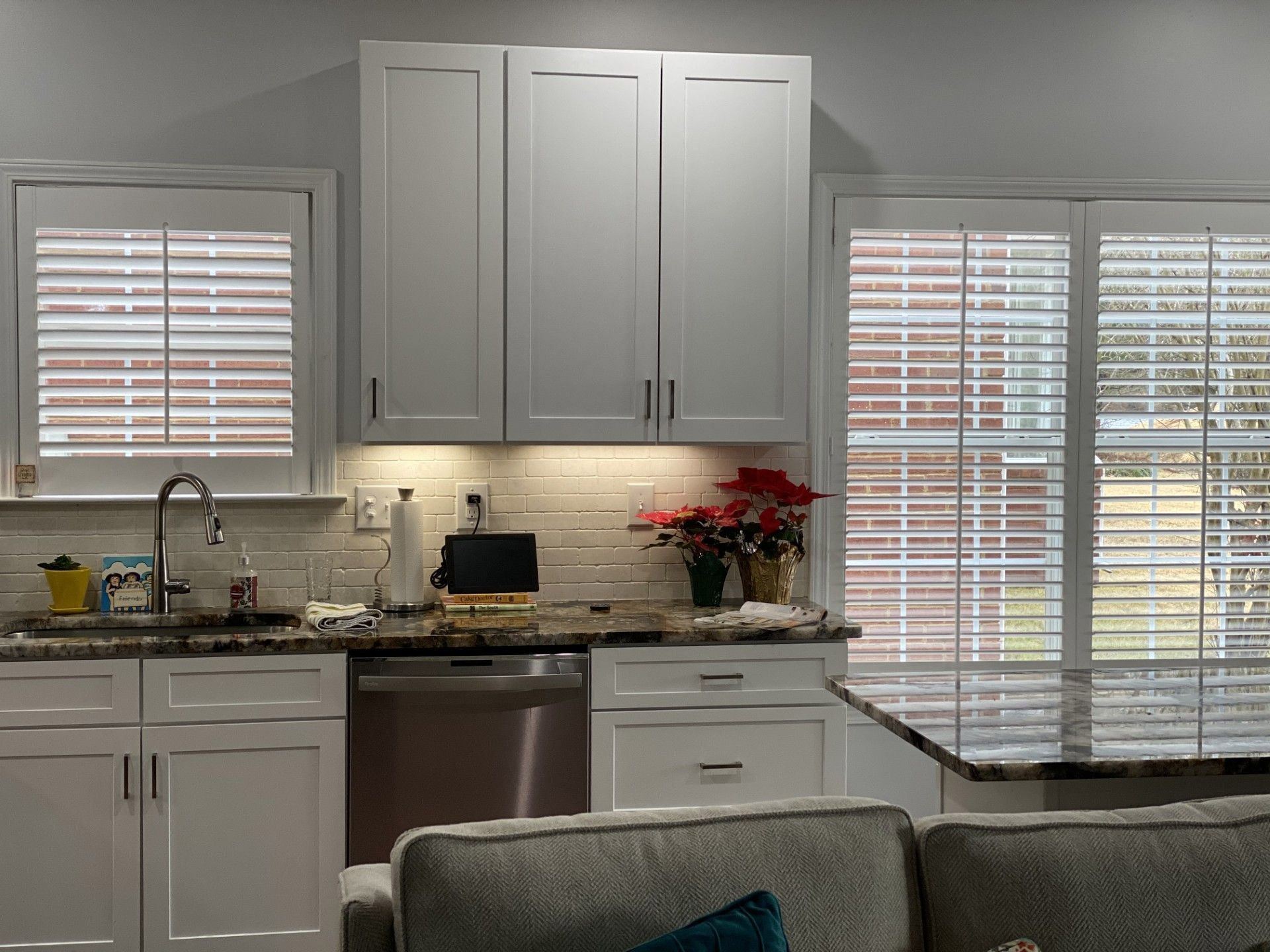 Kitchen with white cabinets, a stainless steel dishwasher, granite countertops, and window shutters.