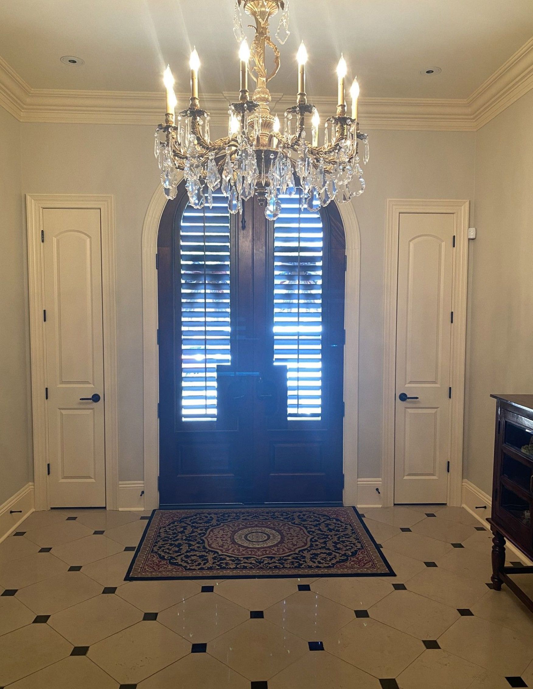 A grand entryway with a double door, flanked by doors on either side, and a large chandelier overhead.