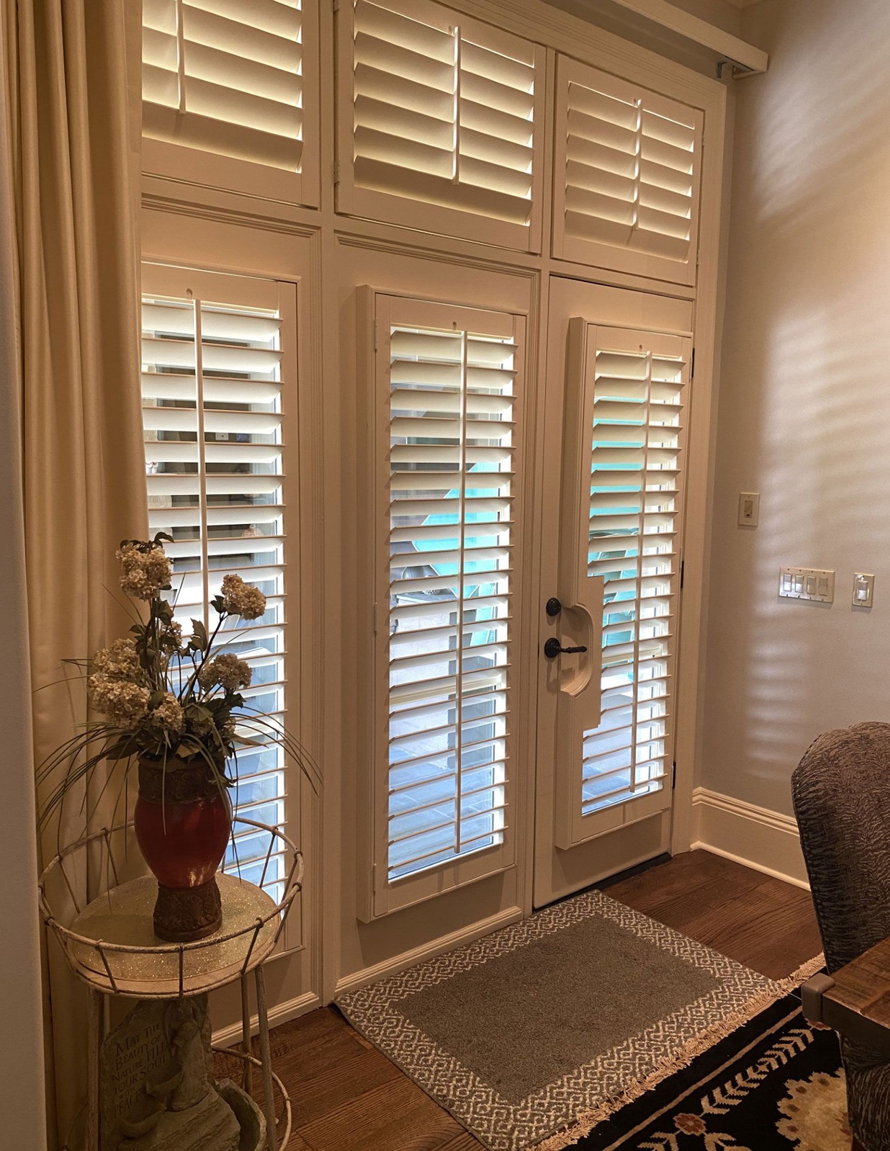 French doors with white shutters and sidelights. A small rug and side table with a vase are in the foreground.