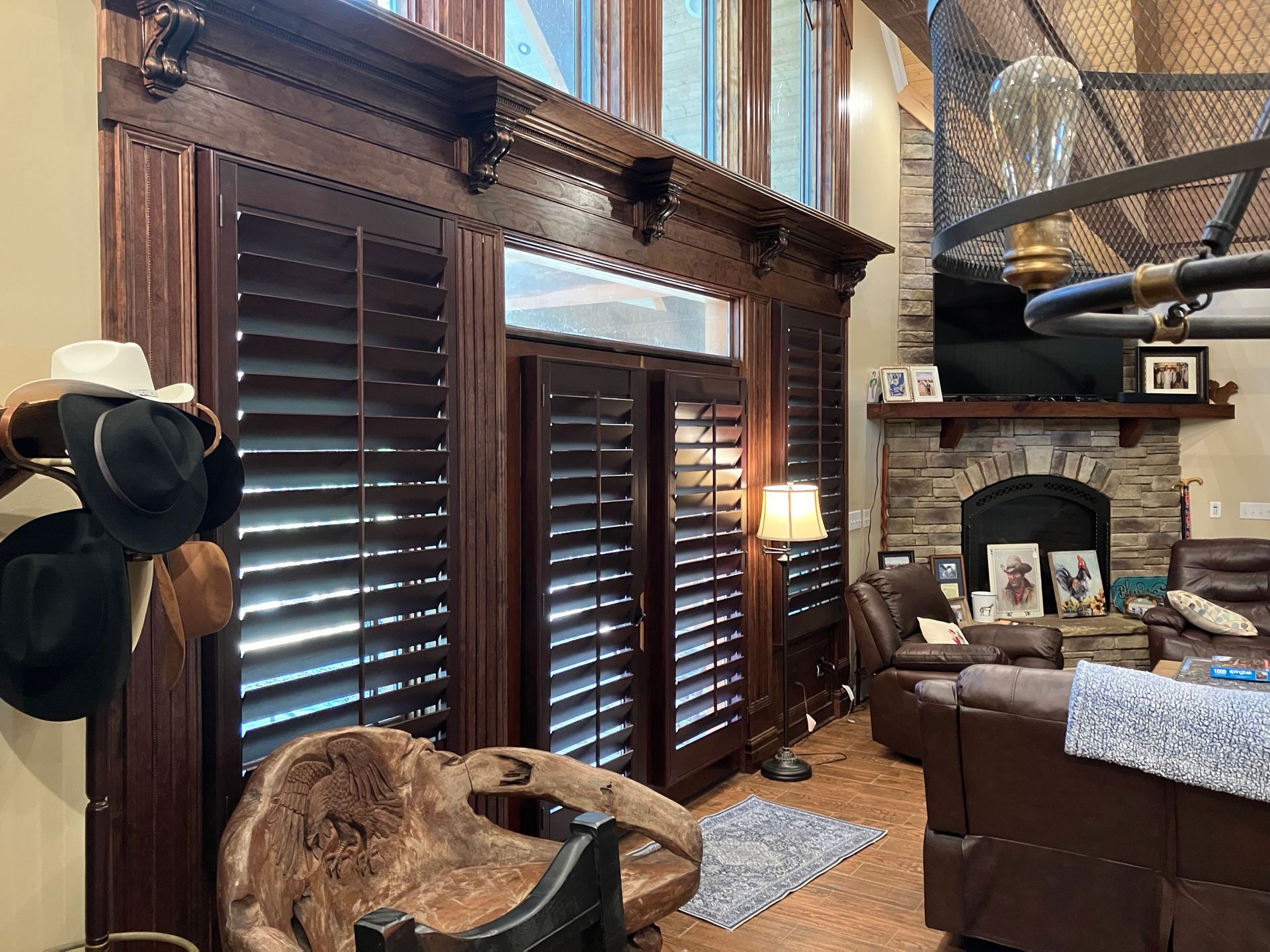 Interior view: Dark wood shutters and trim around windows, a fireplace, and leather furniture. A cowboy hat hangs on the wall.