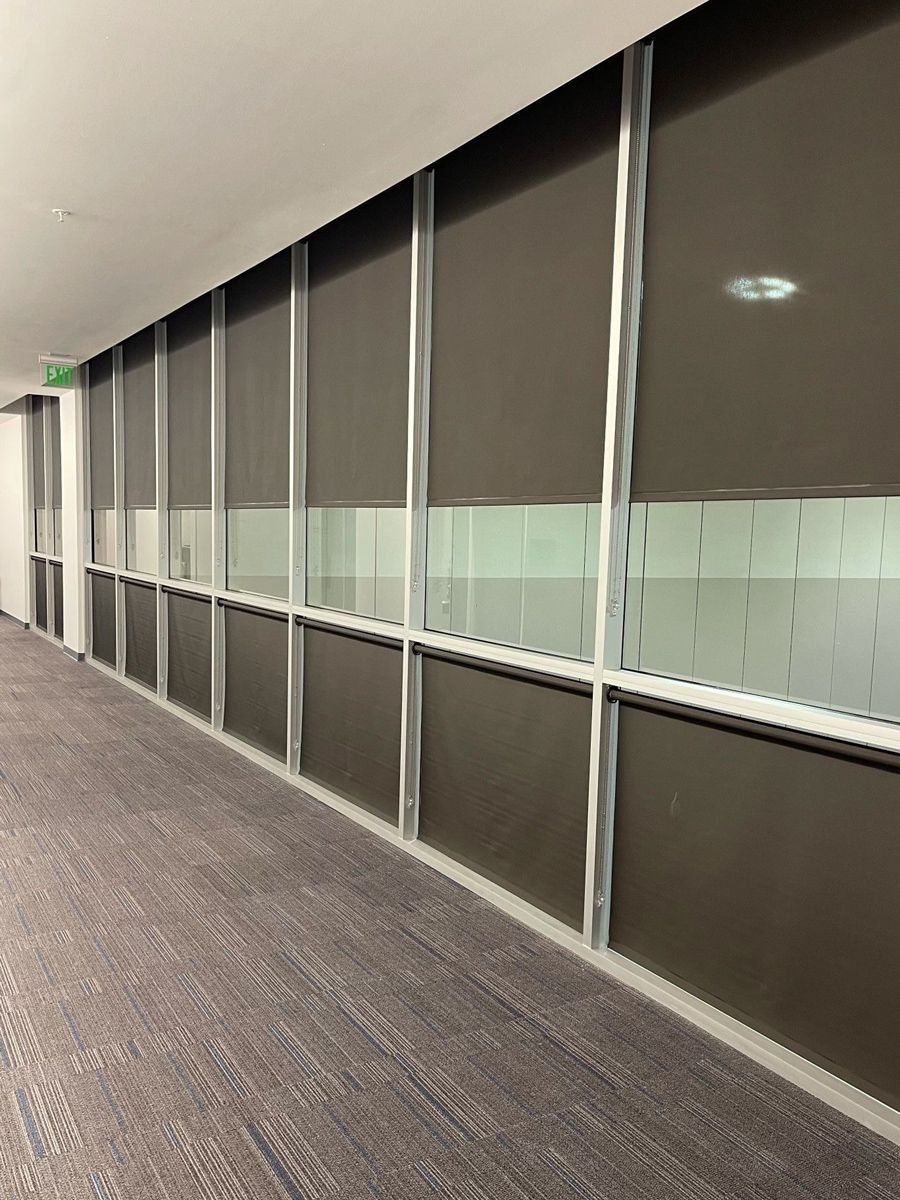 Hallway with large windows covered by dark blinds. Light from the windows illuminates the patterned carpet floor.