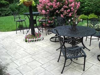 A patio with a table and chairs and flowers in the background.