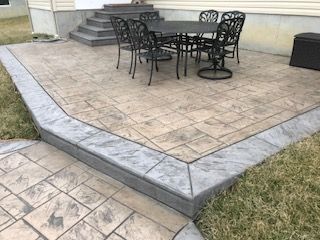 A patio with a table and chairs on it in front of a house.