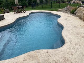 A large swimming pool with a table and chairs in the background.