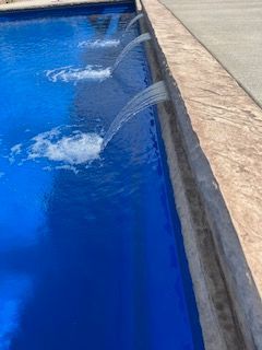 A blue swimming pool with a fountain in the middle of it.