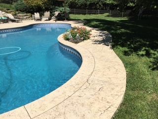 A large swimming pool in a backyard with a concrete deck surrounding it.