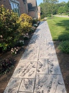 A concrete walkway leading to a house with a lawn in the background.