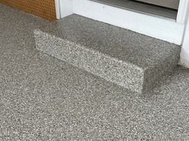 Small gray step on a speckled floor near a doorway.