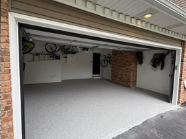 Open garage interior with a light gray floor and white walls, partially open door, and brick side walls