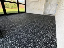 Black speckled epoxy floor in a bright enclosed room with large windows and white walls