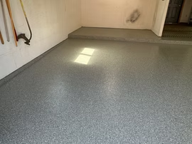 Empty room with speckled gray floor and sunlight patch near the wall