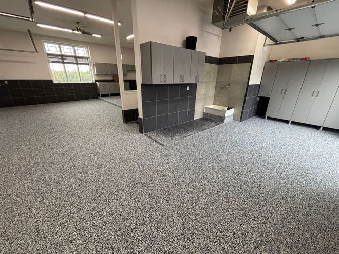 Empty industrial room with gray lockers, black lower walls, and speckled carpet flooring