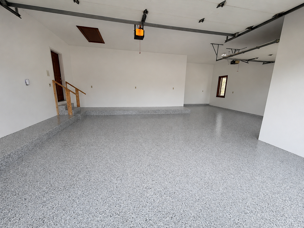 Empty white garage with speckled gray epoxy floor and an open garage door opener overhead