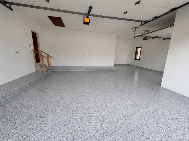 Empty white garage with speckled gray epoxy floor and an open garage door opener overhead