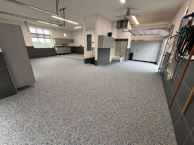 Empty garage-like room with speckled floor, white walls, cabinets, and hanging tools along the right wall.