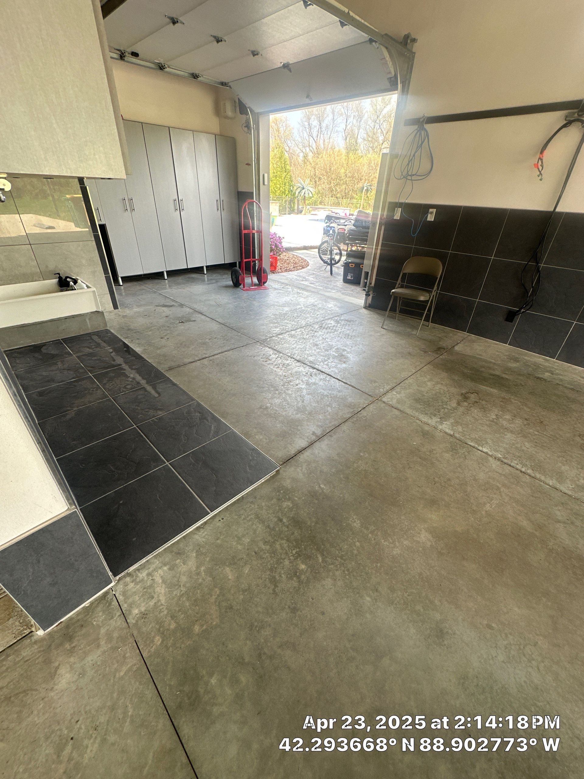 Covered garage/entryway with tiled floor, black wall panels, lockers, and sunlight spilling in from outside.
