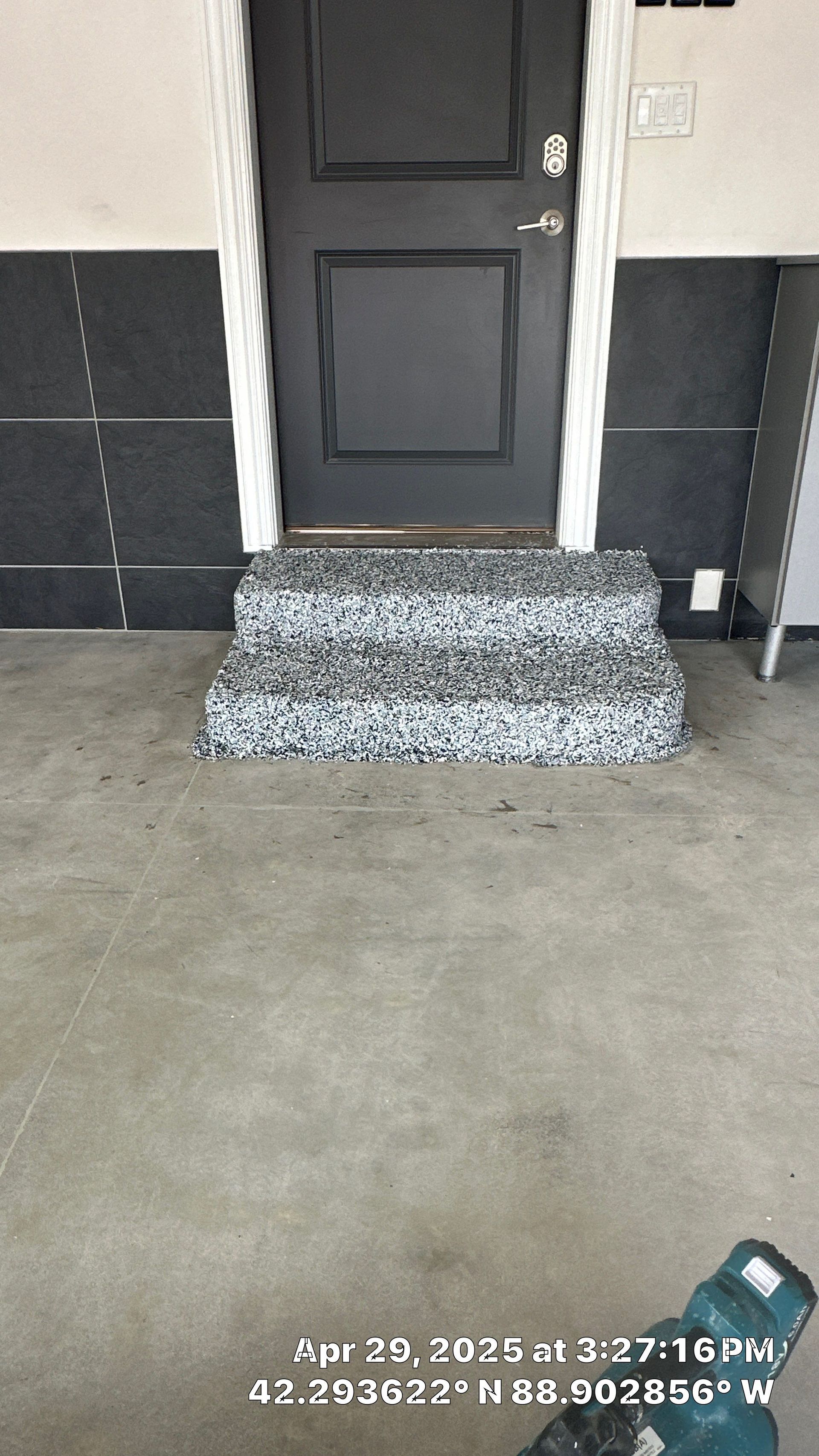 Black door above three speckled stone steps on a concrete porch