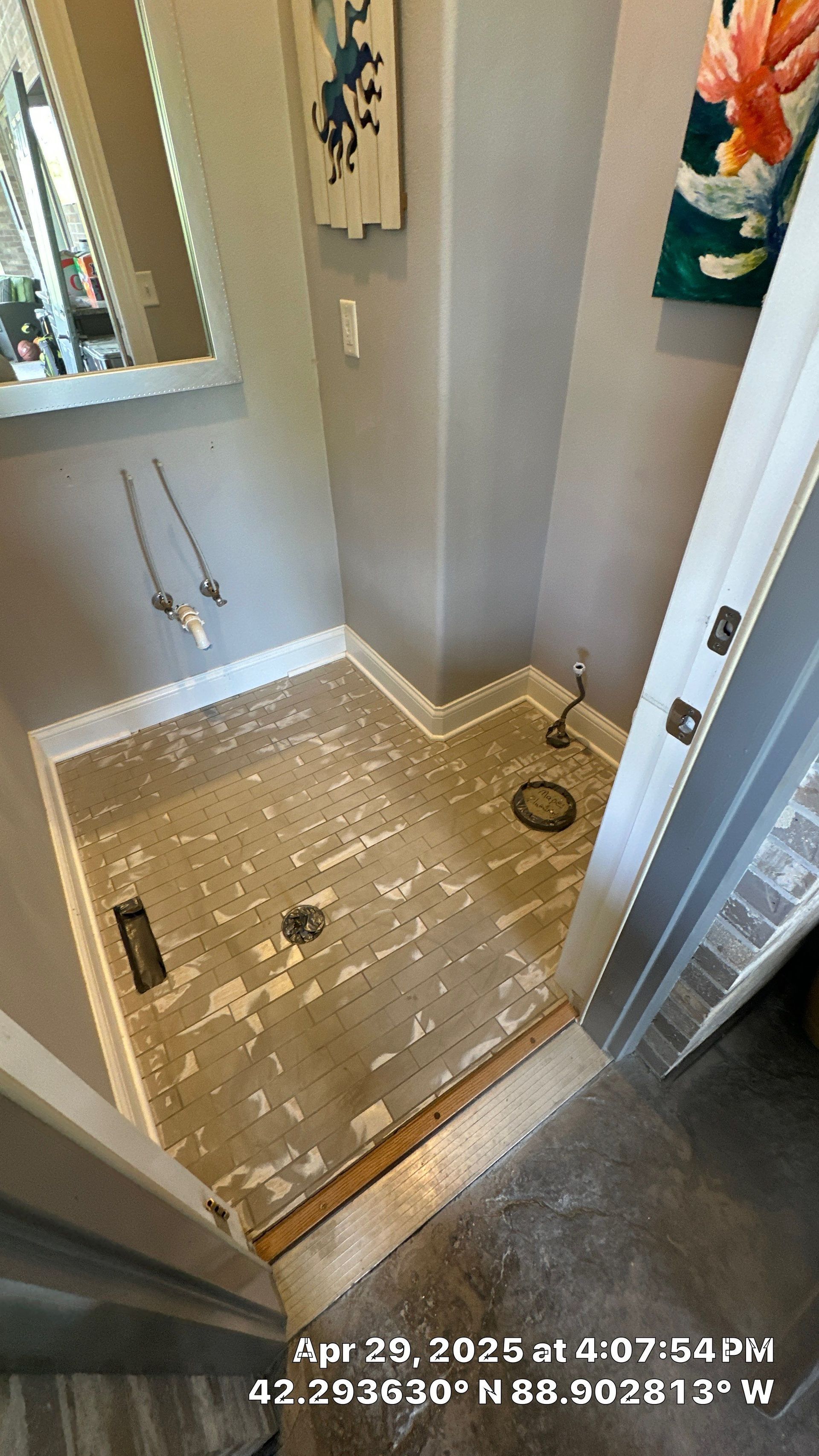 Small bathroom shower floor stripped for renovation, with exposed subfloor and beige walls.