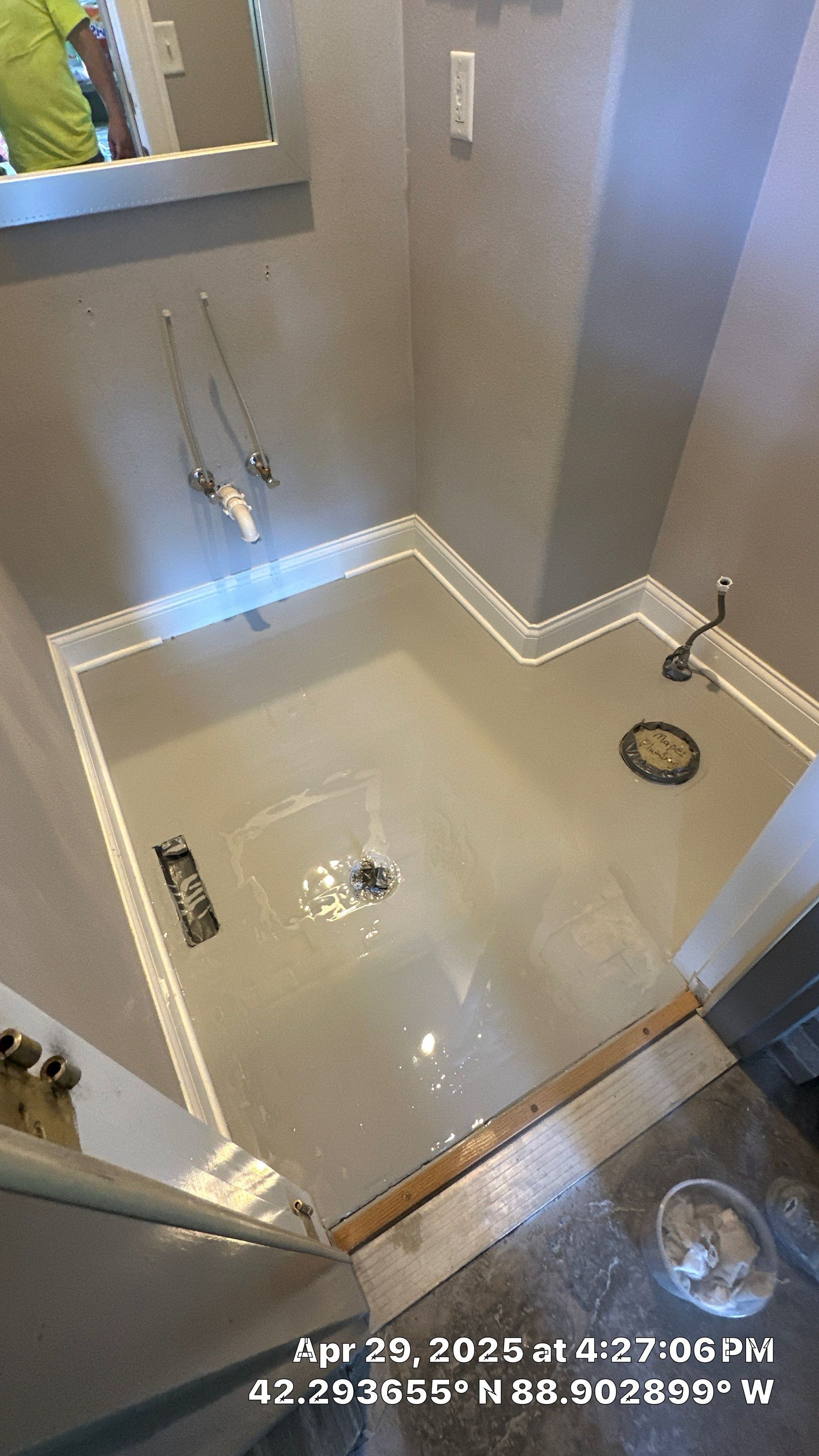 Small beige tiled shower stall with wall shelves, grab bars, and a circular drain.