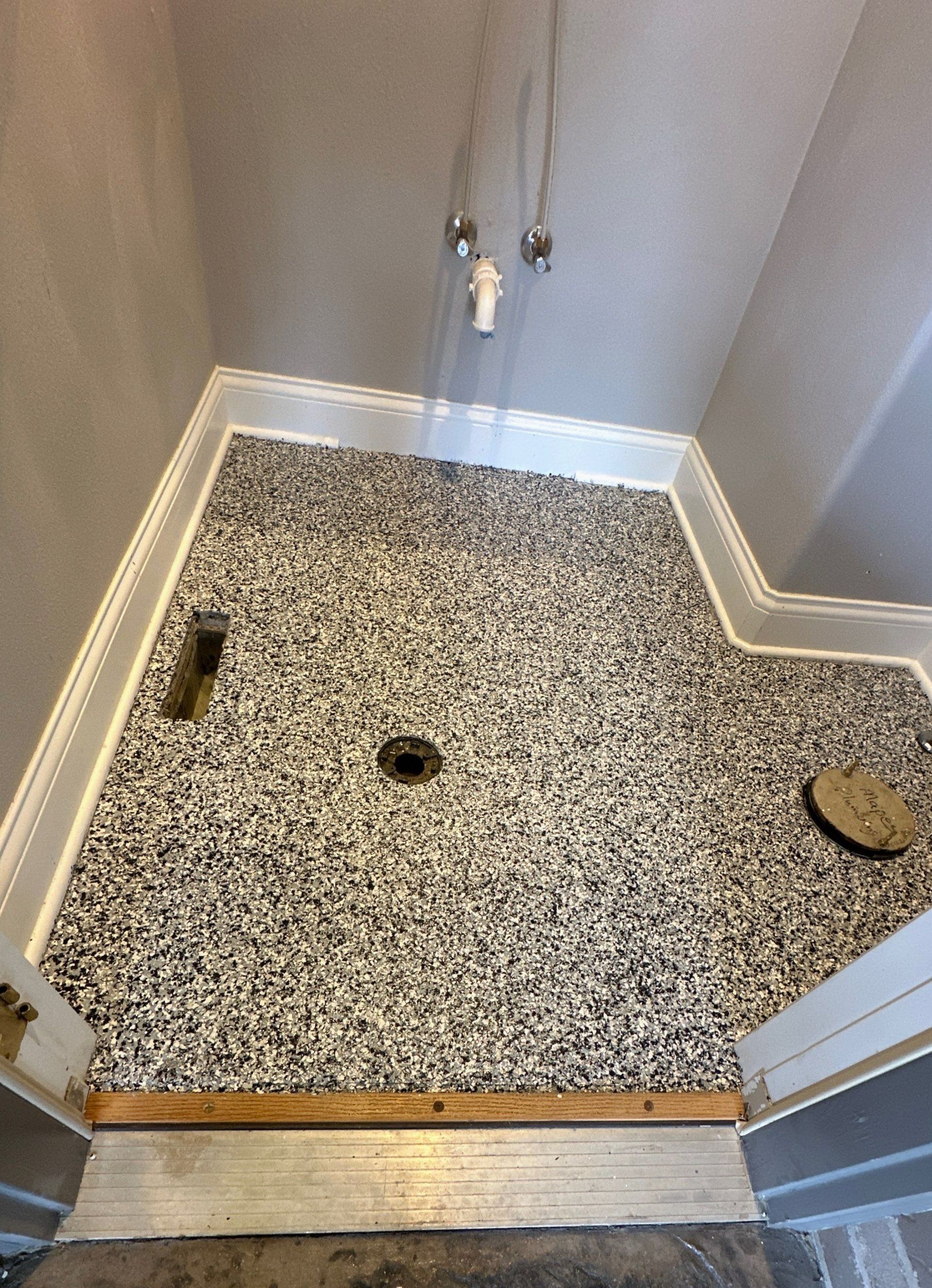 Empty speckled shower floor with drain and plumbing fixtures in a small tiled stall