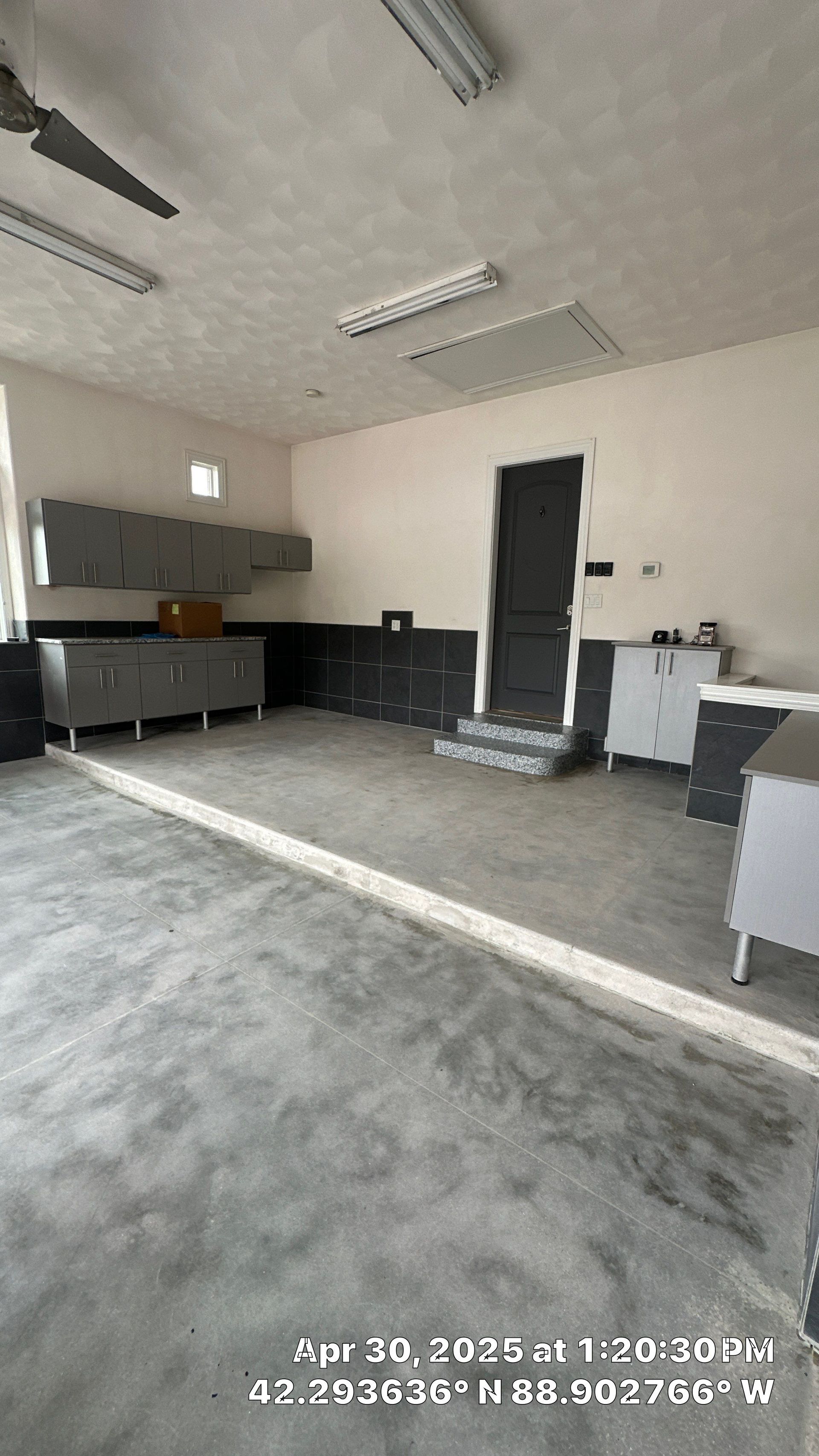 Empty modern garage with gray floor, white walls, cabinets, and a black door.
