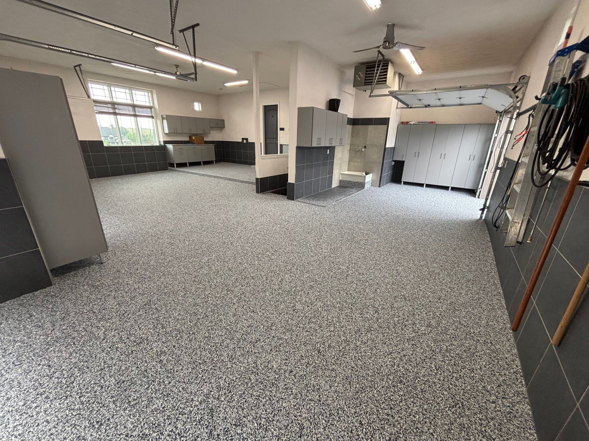 Empty garage-like workshop with speckled floor, gray walls, windows, and hanging tools
