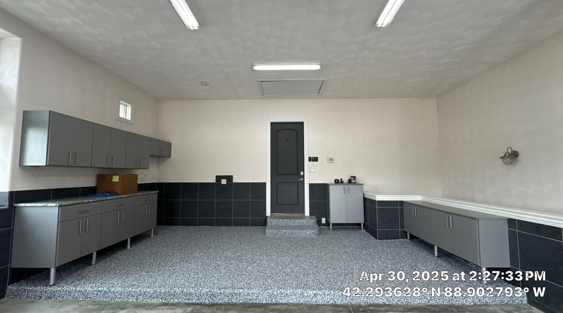 Empty garage with gray cabinets, workbench, dark wall trim, and a central door under fluorescent lights.