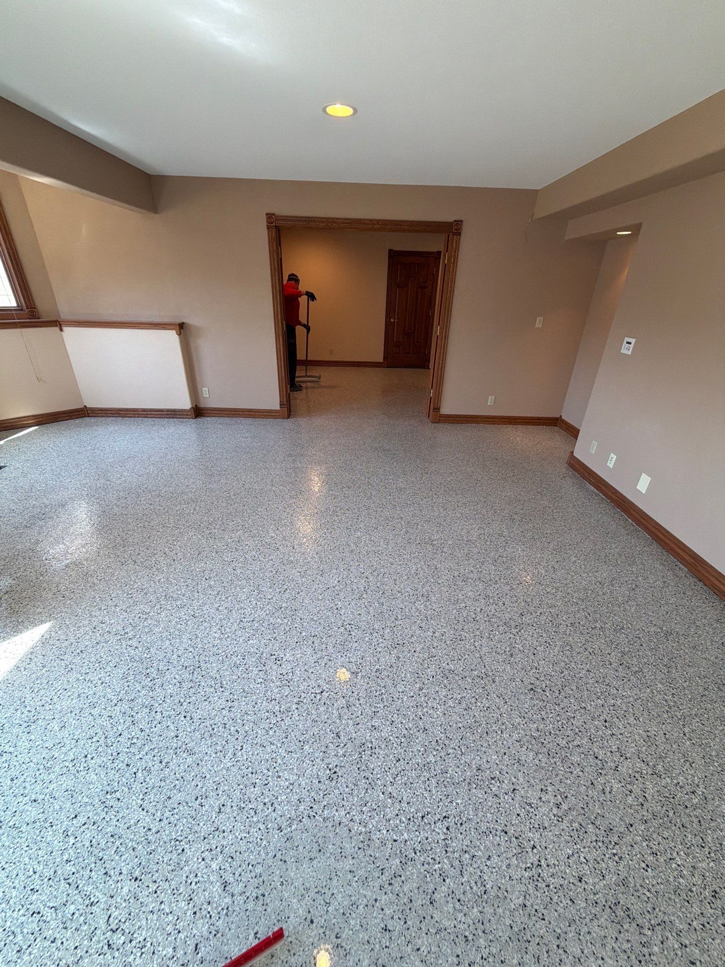 Empty room with speckled floor, beige walls, and a doorway to a hall.