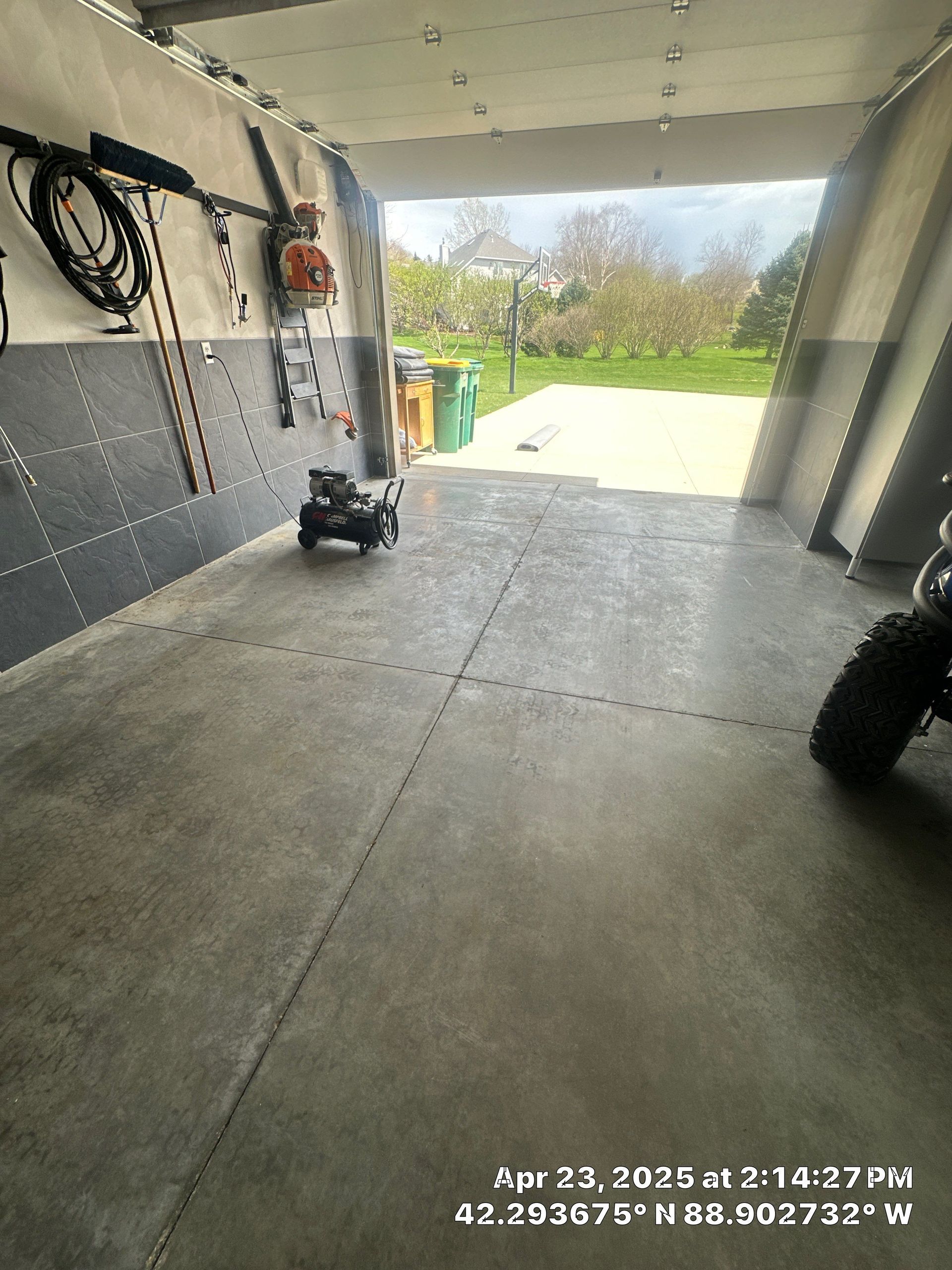 Covered garage or patio with concrete floor, wall-mounted hoses, and a bright view of a backyard outside.