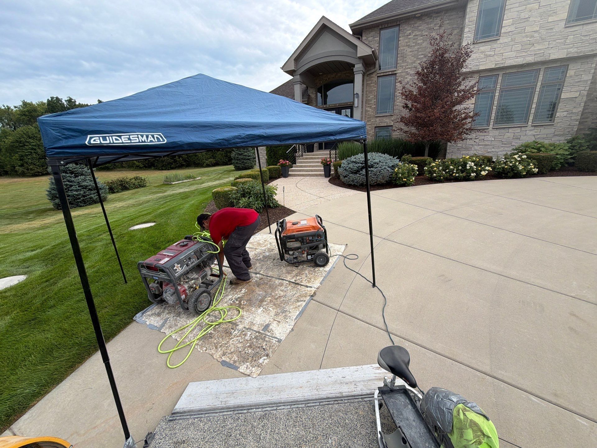 Person using a red tool near a blue canopy on a driveway beside a house