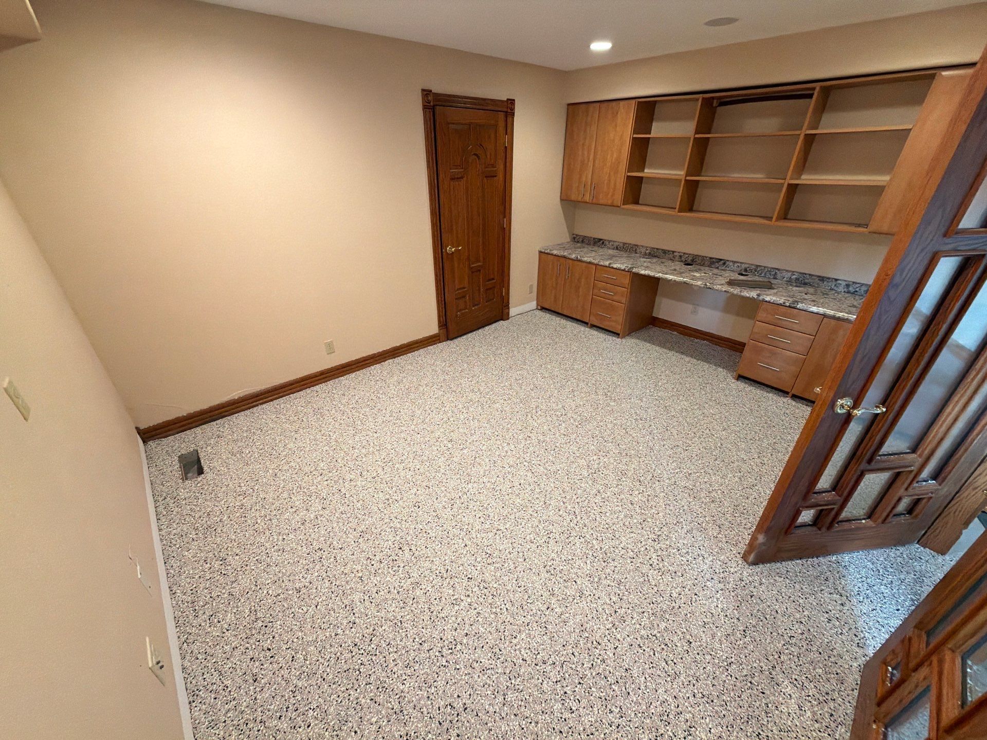 Empty beige room with wood shelving, desk cabinets, and a speckled carpet floor