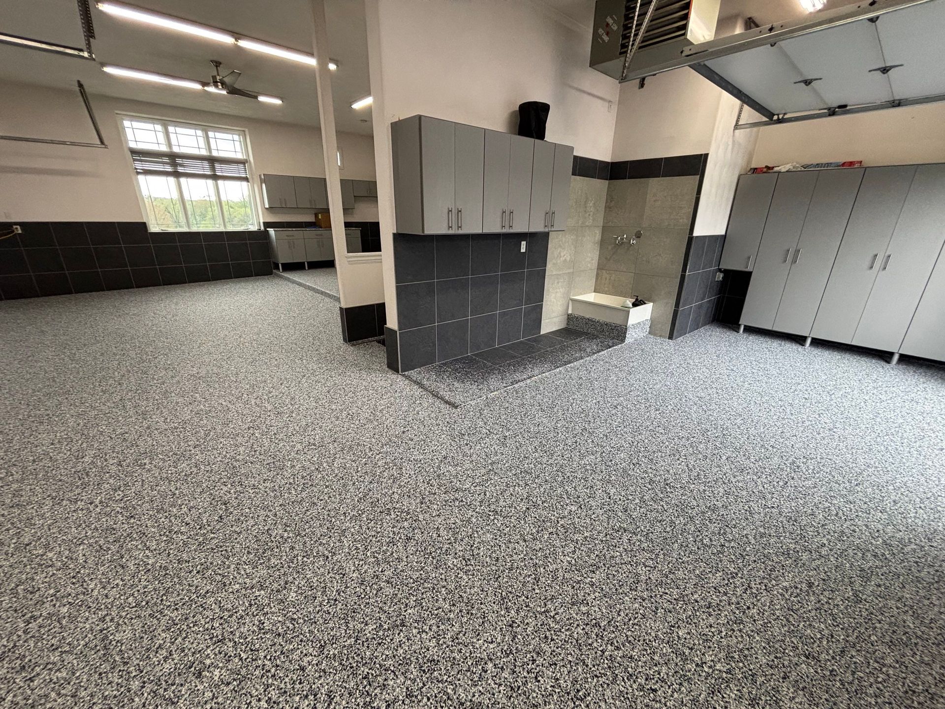 Empty industrial room with gray lockers, tiled walls, and a speckled floor.
