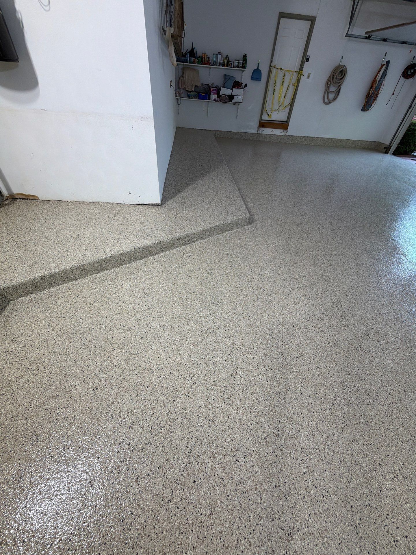 Empty speckled floor in a hallway with a doorway and wall-mounted items in the background.
