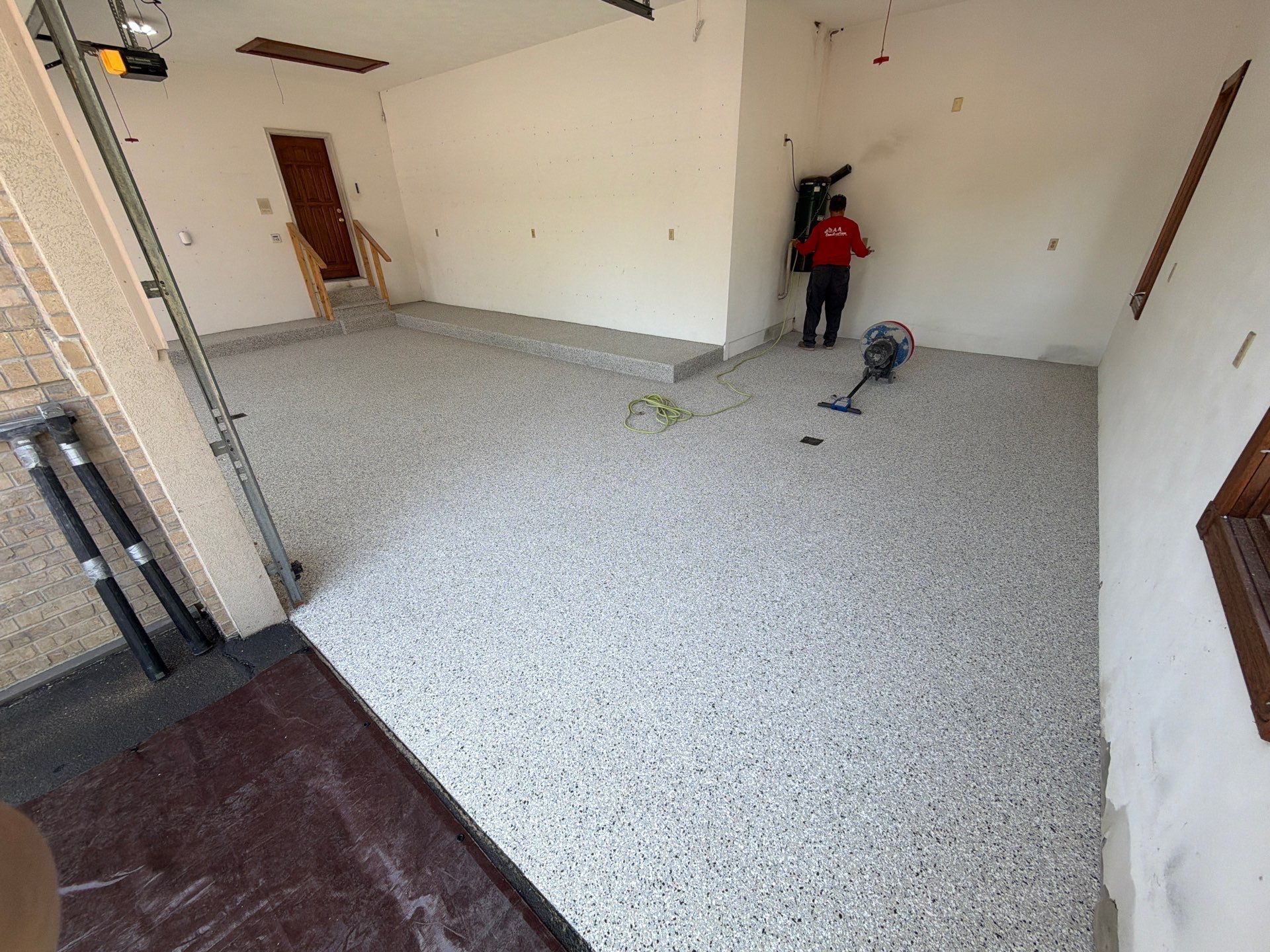 Empty room with gray speckled floor, white walls, and two workers near the back wall.