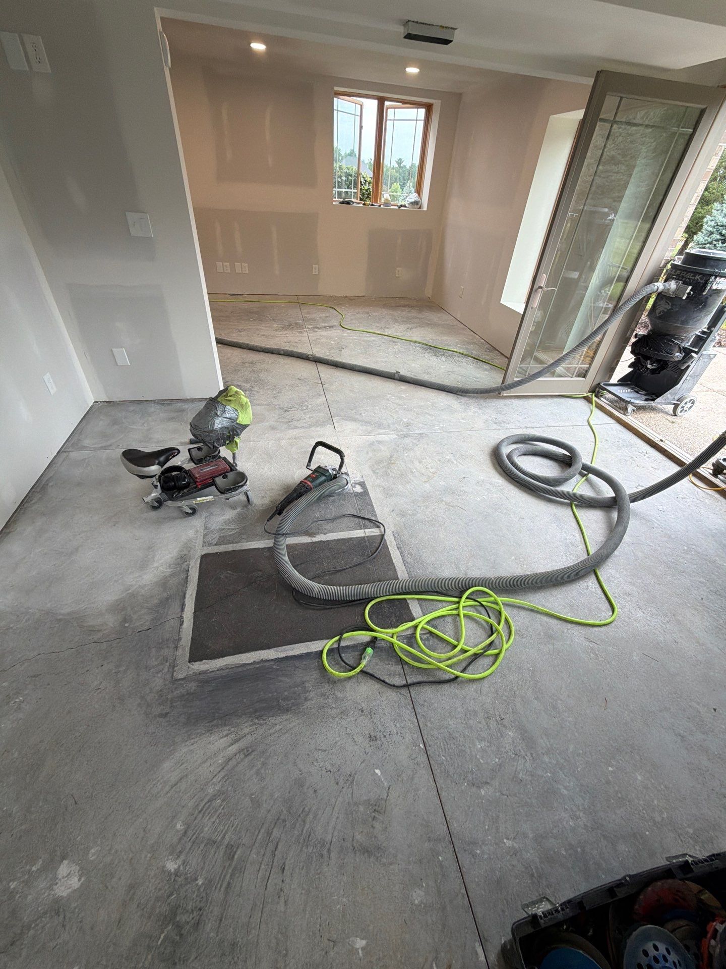 Renovation room with bare concrete floor, tools, hoses, and a floor drain in the foreground.