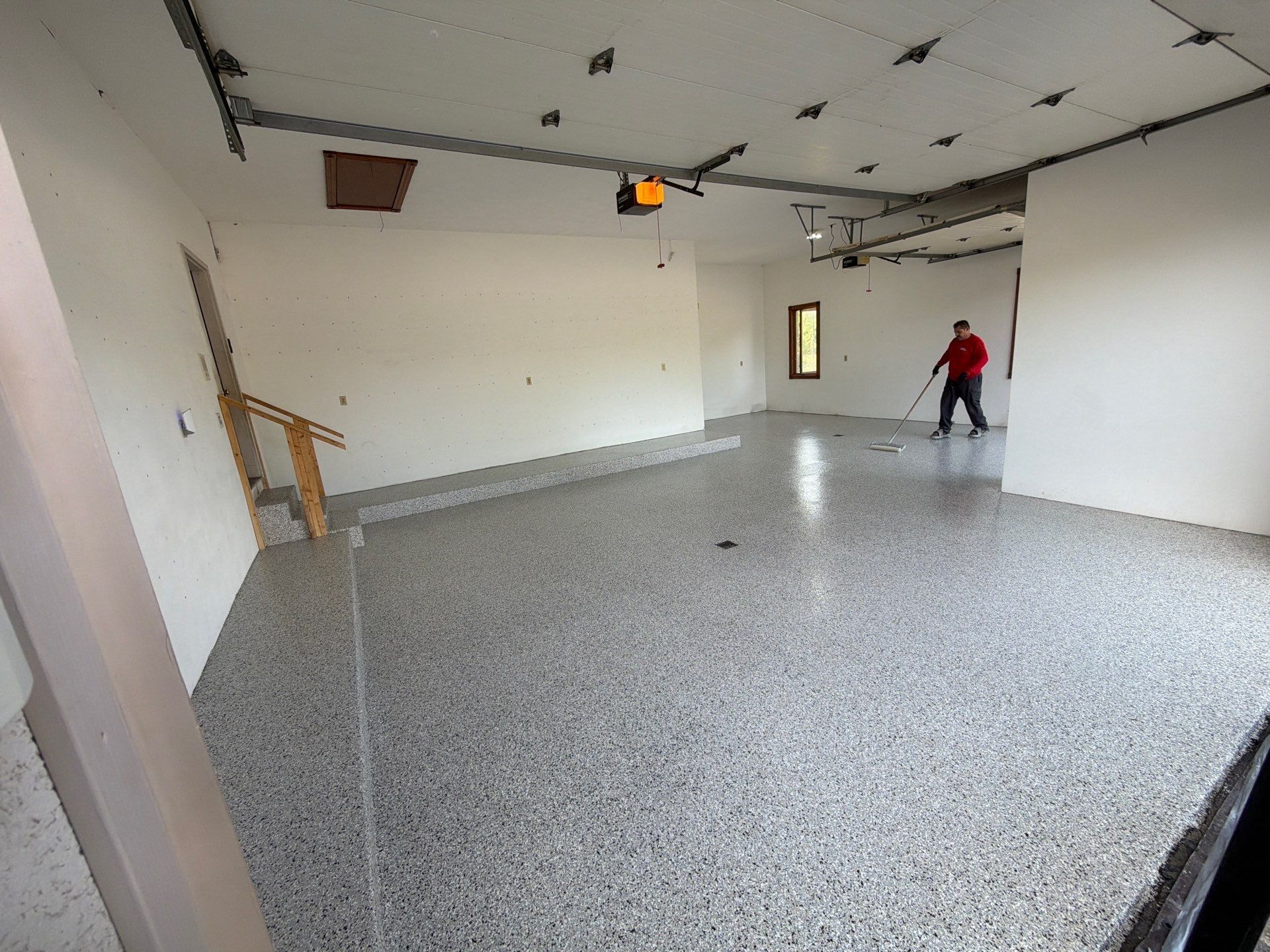 Empty garage interior with speckled floor, white walls, and a person in red near the back wall.