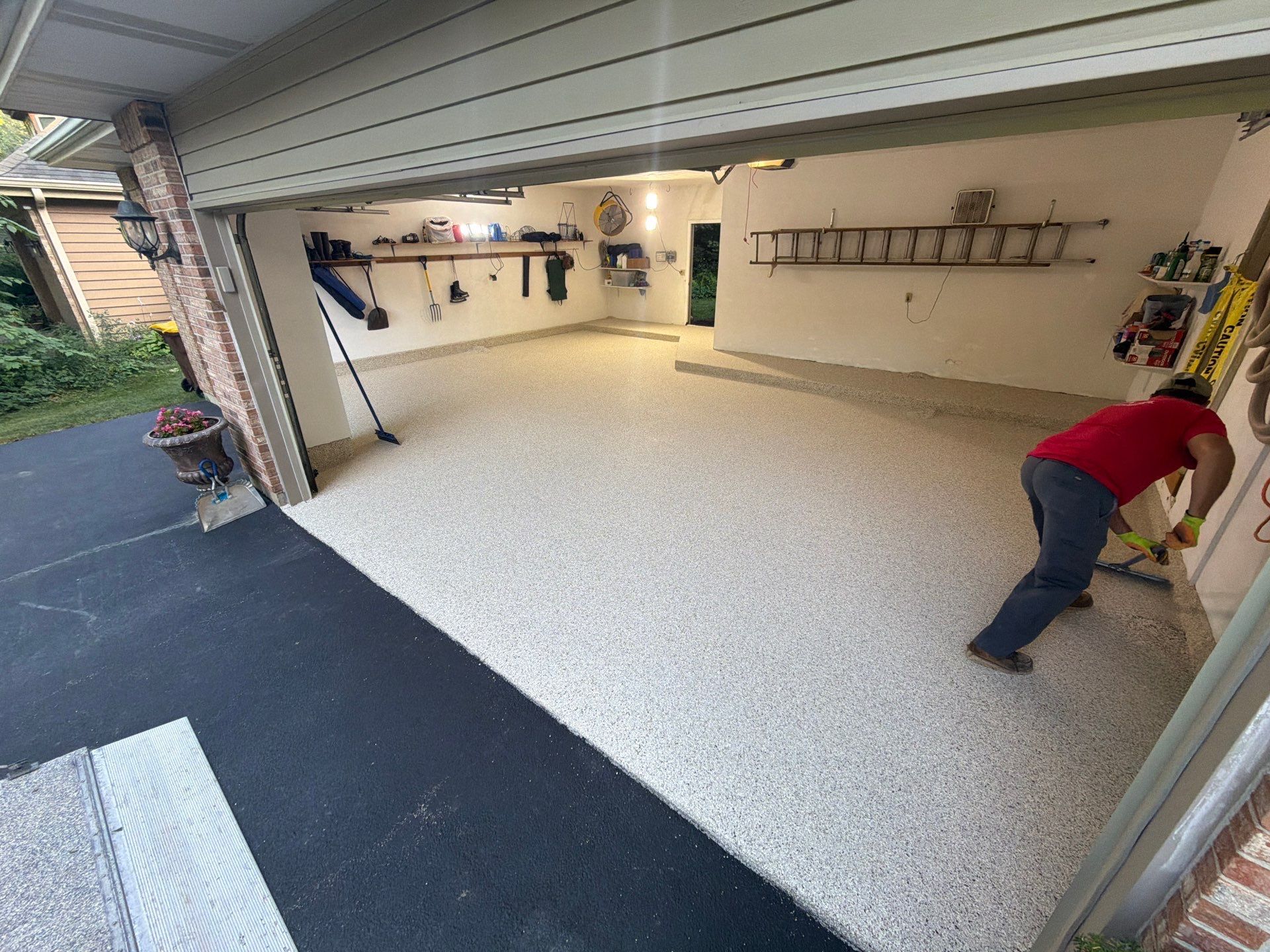 Open garage with speckled floor and wall tools; a person in red is working near the right side.