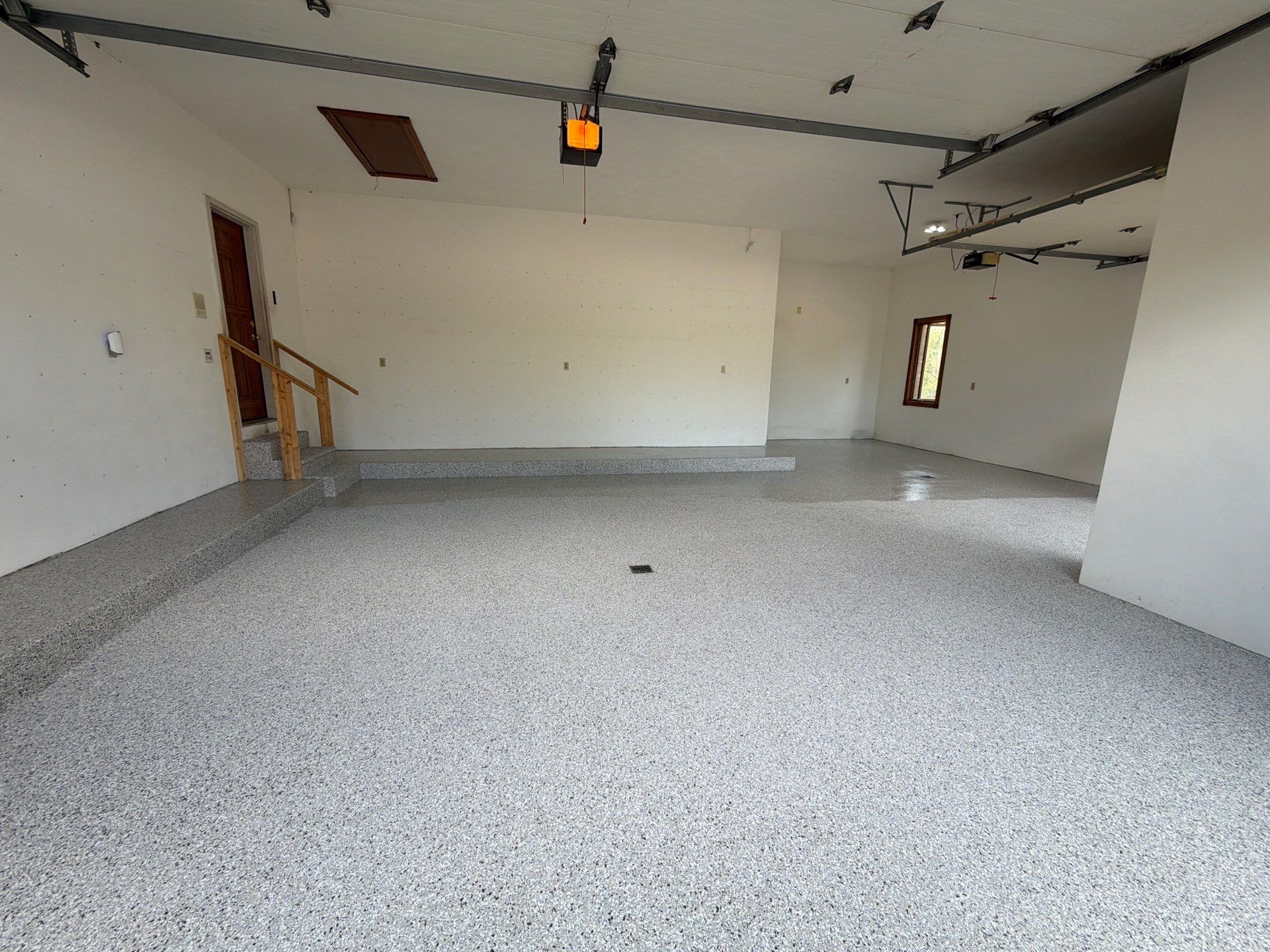 Empty unfinished garage with white walls, gray floor, and a small window.
