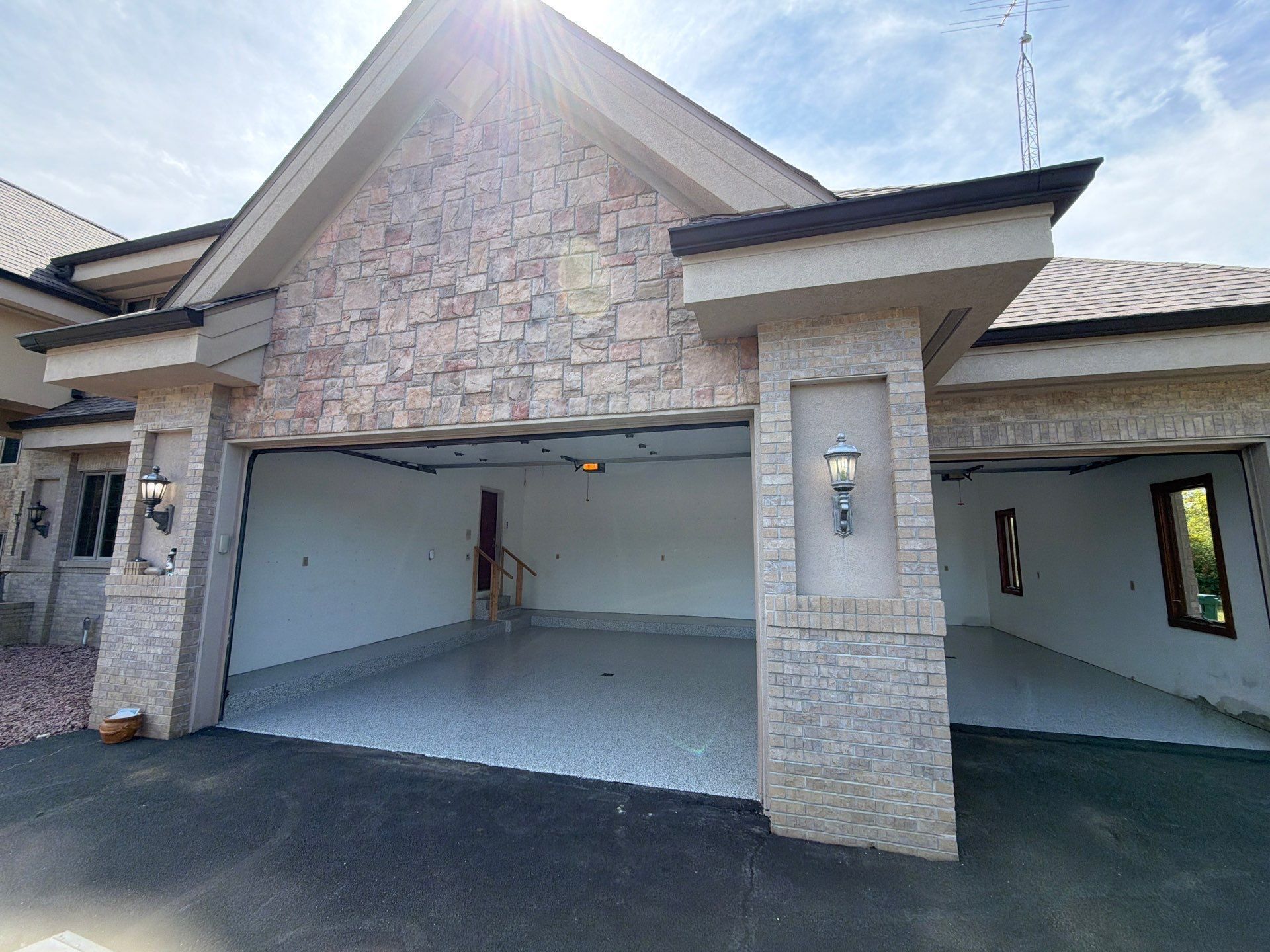Front view of a stone-and-stucco house with an open two-car garage under a bright sky