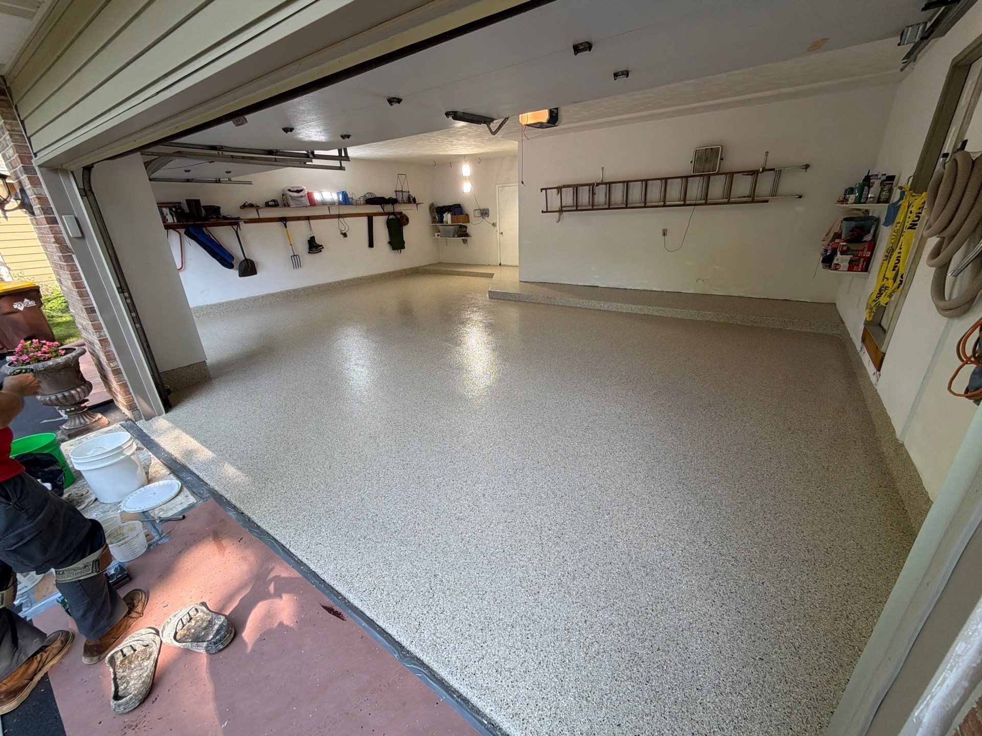 Empty garage with speckled epoxy floor, wall shelves, and hanging tools.